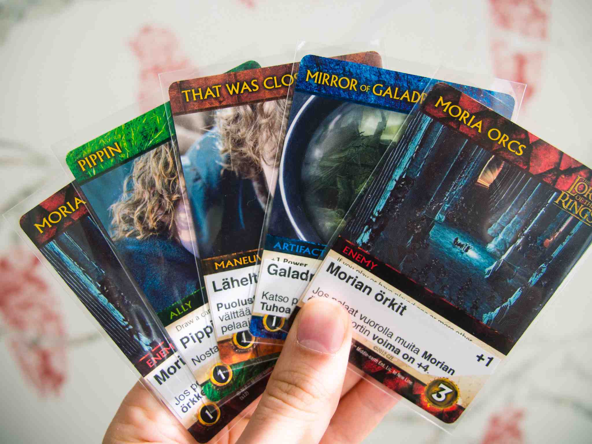 a person's hand holding 4 lord of the rings cards